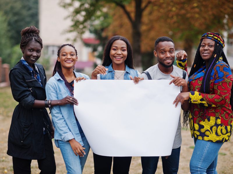 Group of five african college students on campus at university yard hold empty white blank. Free space for your text. Black afro friends studying.